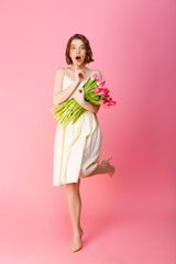 young shocked woman with bouquet of pink tulips isolated on pink