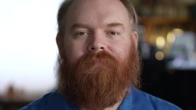 Black look on the face of man with red thick beard as he stares into the camera.