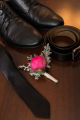 Groom’s accessories: a part of black shoes in focus, flower boutonniere, leather belt, necktie. Wedding