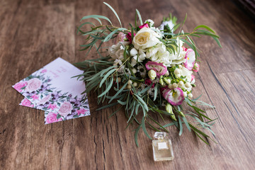Lush bridal Bouquet with white roses and a lot of greenery and a few invitations lying on the wooden floor. Wedding