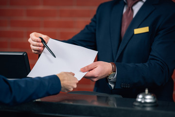 cropped shot of hotel receptionist giving contract to customer