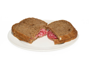 Two sandwiches of whole grain bread with slices of sausage on a white plate