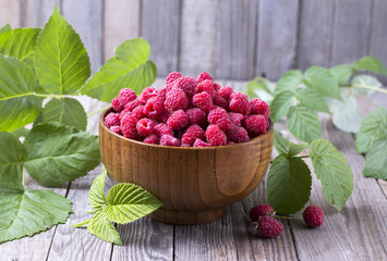 Red fresh raspberries on brown rustic wood background. Bowl with natural ripe organic berries with peduncles, green leaves