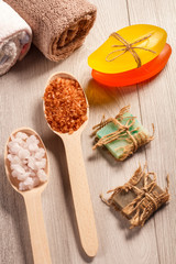 Wooden spoons with white and brown sea salt and handmade soap for bathroom procedures with towels on the background