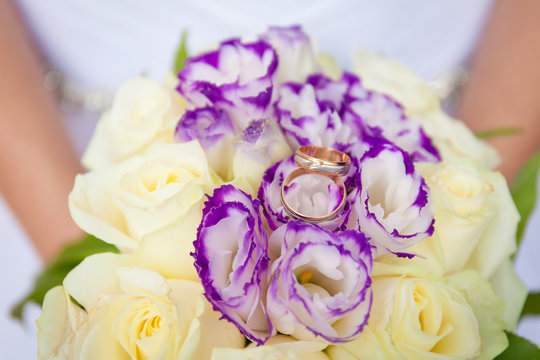 Wedding flowers. Beautiful fresh small new round bouquet of different colors, golden rings of the newly-married couple on top. Beautiful photo for web sites and postcards.