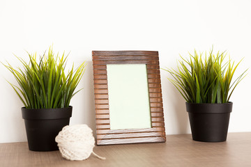 Wooden photo frame next to two pots of grass over white background