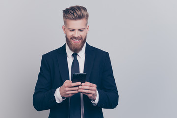 Portrait of handsome with stylish hairdo cheerful funny excited financier using smartphone playing online games receiving getting writing sms updating his digital gadget isolated on gray background