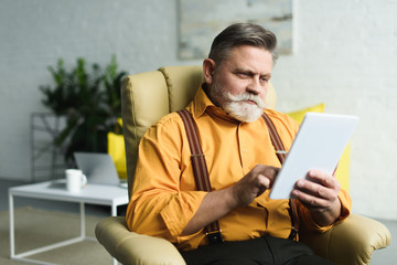 handsome bearded senior man using digital tablet at home