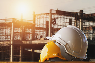white and yellow safety helmet in construction side with sunset - obrazy, fototapety, plakaty