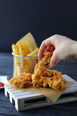 Woman hand holding crispy chicken strips with french fries islated on black background - fast food concept with KFC crispy strips 