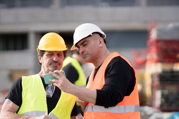 Construction workers at work on construction site using an electronic device. Outdoors