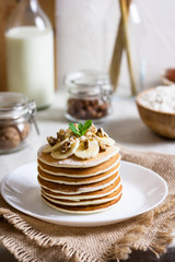 Stack of delicious pancakes with chocolate, honey, nuts and slices of banana and stawderry jam on plate and napkin on wooden background