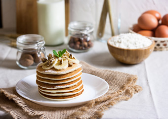 Stack of delicious pancakes with chocolate, honey, nuts and slices of banana and stawderry jam on plate and napkin on wooden background