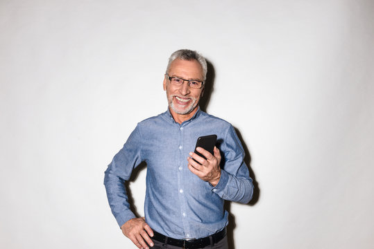 Cheerful mature man smiling and holding smartphone isolated