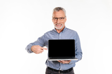 Happy mature man pointing at blank screen of laptop computer isolated