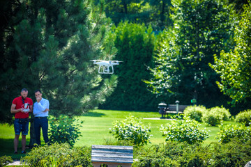 Compact drone hovers in front of two hipster men. Quad copter flies near pilot. Farmer and...