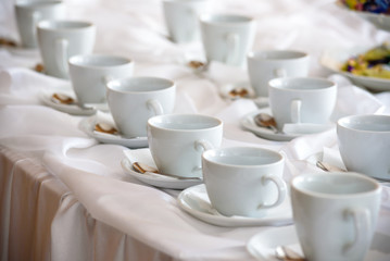 Many white coffee cups in a line over a buffet