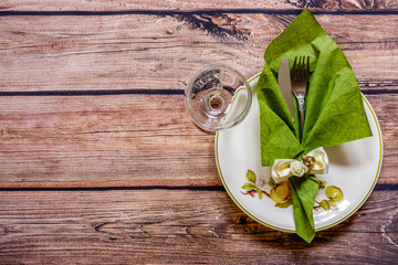 Vintage silverware on a green napkin on a plate and wineglass on wooden background