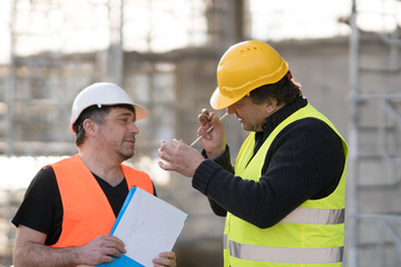 Two happy civil engineers wearing protective vests and helmets at work on construction site