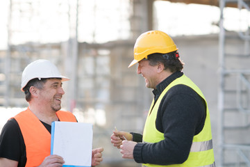 Two happy civil engineers wearing protective vests and helmets at work on construction site