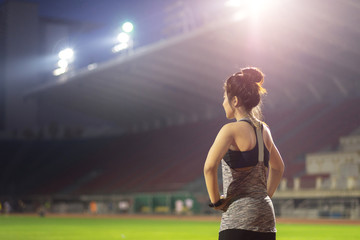 young female athlete stretching before running on grass in football stadium at night