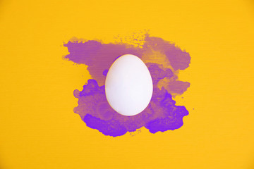 One white egg on bright yellow background with violet watercolor splatters.