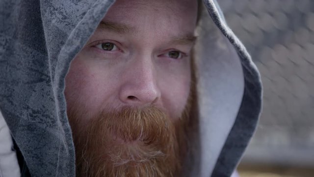 Close up of homeless mans face wearing hoodie trying to keep warm from the cold.