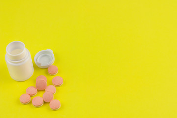 Heap of double color whole pills beside plastic container and cap on background of yellow paper