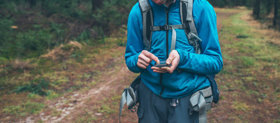 Young male backpacker with smartphone on forest path.