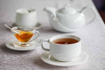 White cup of tea with honey on a white background with teapot. Serving tea. Honey in Saucer.