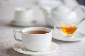 White cup of tea with honey on a white background with teapot. Serving tea. Honey in Saucer.