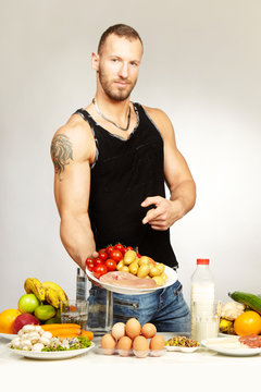 Muscle fitness man posing with his healthy food menu on plates