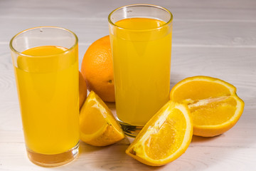 Glass of orange juice and fresh oranges on white wooden table