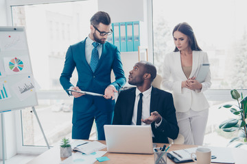 Obraz premium Three thoughtful, stylish, attractive, confident, elegant directors working in work place, station, holding clipchart, gesturing with hand, explaining, having debate, dispute, finding solution