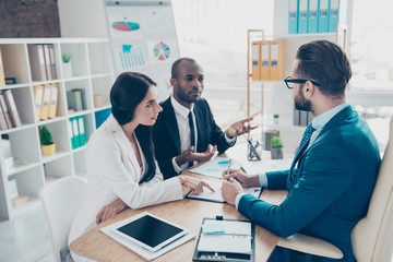 Obraz premium Three serious, concentrated, successful, elegant businesspeople in classic suits are going to make a deal, sign a contract, sitting in work place, station, discussing details of paper