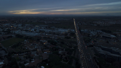 Aerial sunset view of an industrial area of a large Italian city with warehouses, warehouses, offices and buildings. Among the asphalt roads beyond the cars, vans and trucks there are trees.