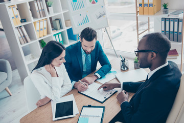 Happy couple is making a success deal about their business, young bearded attractive afroamerican lawyer in classic suit is presenting contract to sign, sitting workplace, workstation