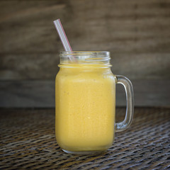 Fresh organic mango shake in glass mug on wooden table, close up