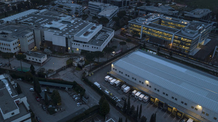 Aerial night view of an industrial area of a large Italian city with warehouses, warehouses, offices and buildings. Among the asphalt roads beyond the cars, vans and trucks there are trees.