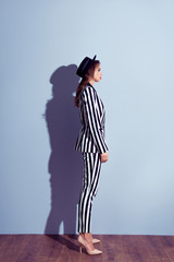 Full-length profile side view portrait of charming thinking pensive dreamy beautiful rich luxurious concentrated elegant graceful woman clothed in striped dress-code with cap isolated gray background
