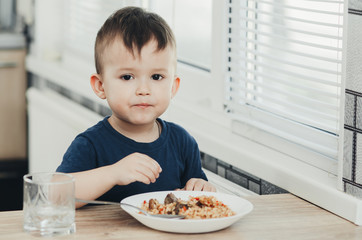 beautiful cute baby eats rice with a spoon in the kitchen, very fun