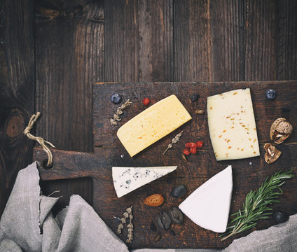 pieces of different cheeses on a brown wooden board: brie, roquefort, cheese with nuts