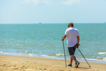 Active senior man walking with nordic walking poles on the beach