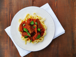 Neapolitan ragu with tagliatelle pasta on plate over wooden table, top view.