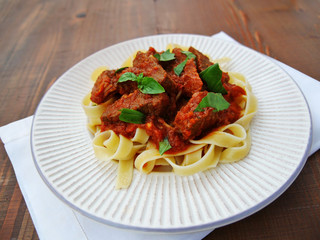 Neapolitan ragu with tagliatelle pasta on plate over wooden table.