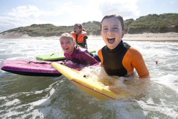 Three girls are smiling for the camera as they bodyboard in the sea together.