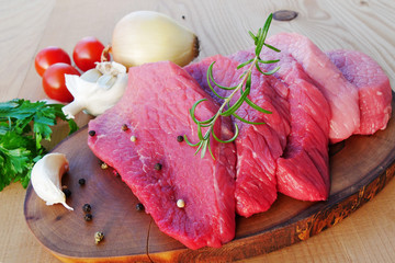 Sliced red meat on wooden board with herbs and spices. Veal beef slices ready for schnitzel or barbecue.