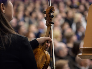 A violin in the hand of a musician in the background of a concert hall.