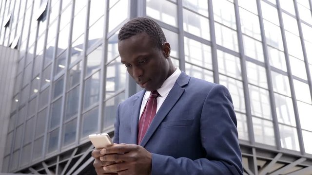 handsome African Black young man in the street tyoing on his smartphone- outdoor