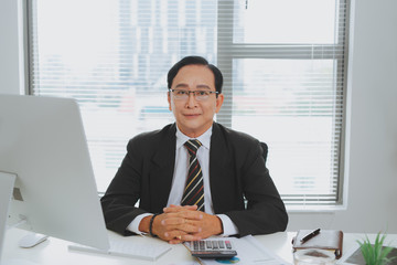 Confident senior asian business leader sitting at desk.